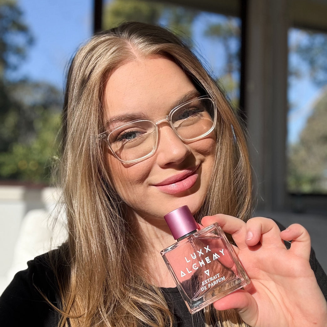 Woman holding a perfume bottle outdoors with trees in the background